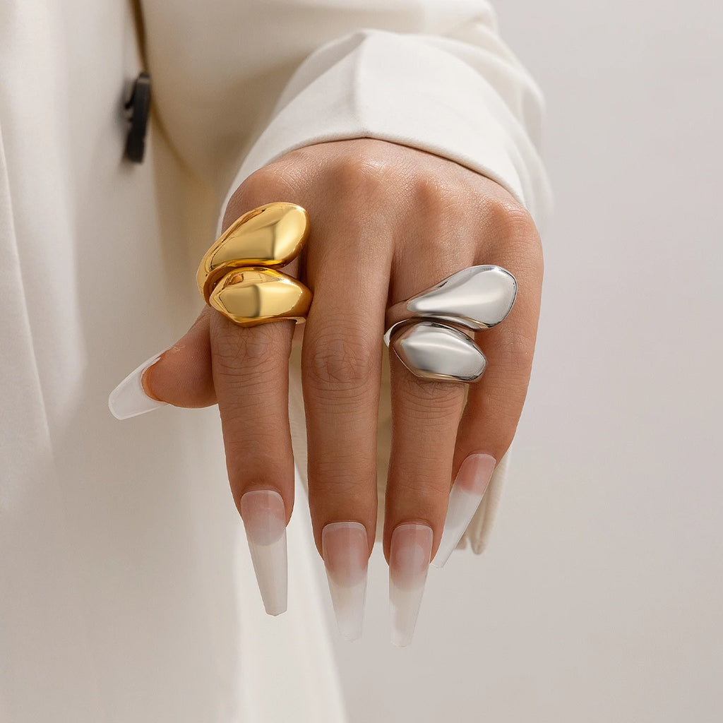 Hand wearing two rings, one gold and one silver, on a neutral background