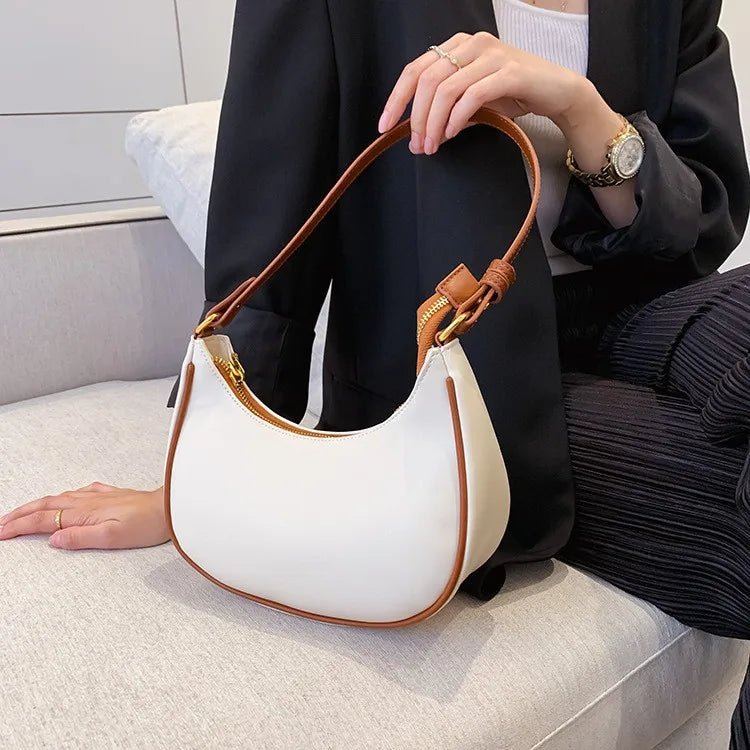 Person holding a white handbag with brown leather accents on a light-colored surface.