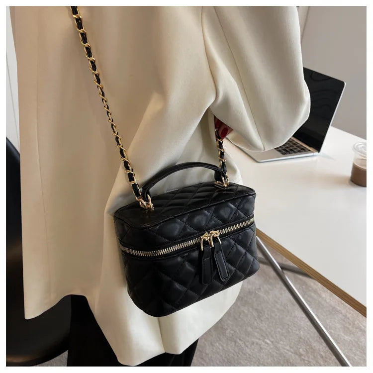 Black quilted handbag with gold chain strap worn by a person sitting at a desk.