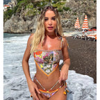 Woman in a colorful swimsuit standing on a rocky beach with ocean waves.