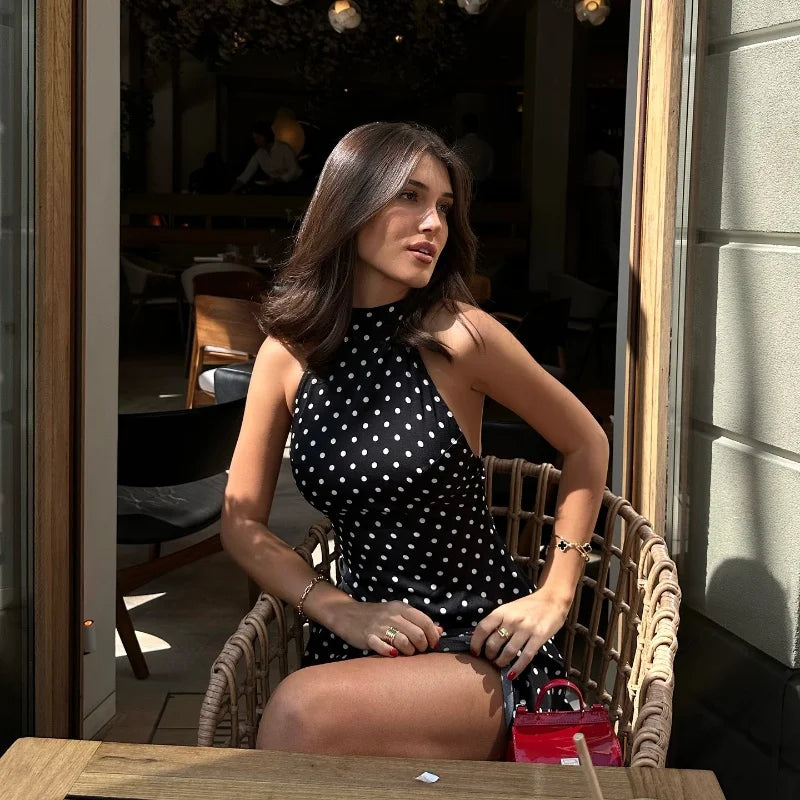 Woman in a black polka dot dress sitting at an outdoor cafe.