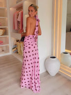 Woman in a pink polka dot dress standing in a stylish room with shelves and decor.