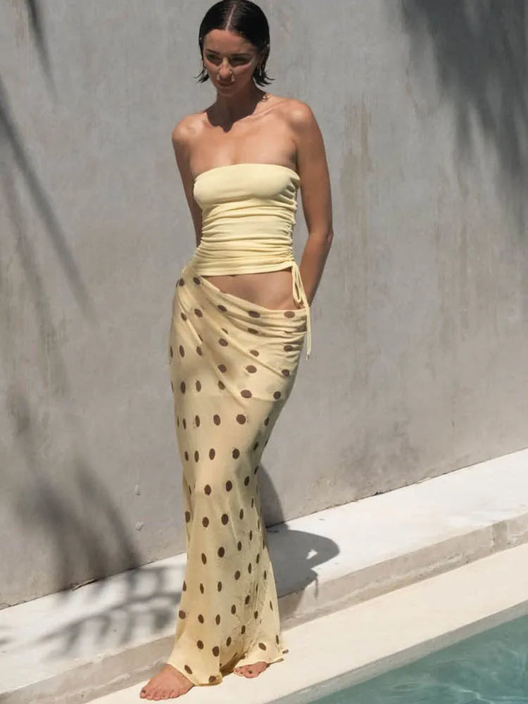 Woman wearing a strapless yellow top and polka dot skirt by a pool.