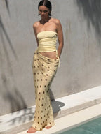 Woman wearing a strapless yellow top and polka dot skirt by a pool.