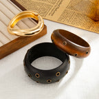 Three bracelets in gold, black, and brown on a textured surface with a newspaper in the background.