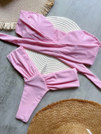 Pink swimsuit laid out on a textured surface with woven mats.