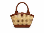 A structured handbag with a natural woven cane body and brown leather trim, featuring dual top handles and a front strap closure, shown against a plain white background.