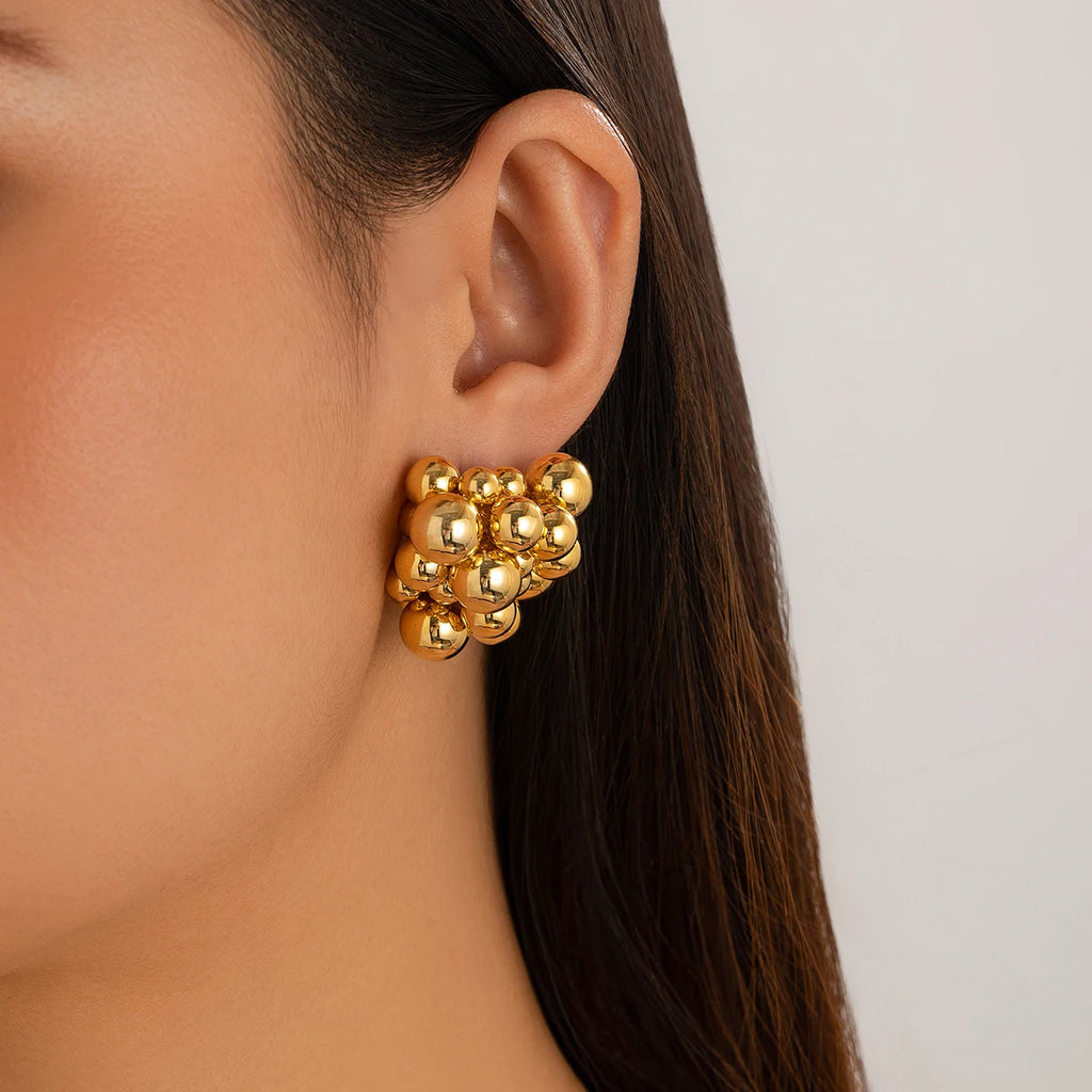 Gold bead earring worn by a person with a neutral background
