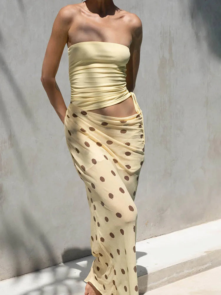 Woman wearing a strapless, beige dress with brown polka dots against a gray background