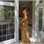 Woman in a floral dress standing in a sunlit room with large glass doors.