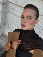 Woman holding a beige clutch against a stone wall background