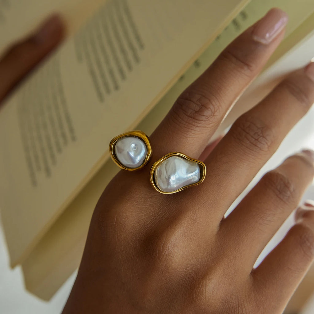 Gold rings with pearl-like stones on a hand, with a blurred background