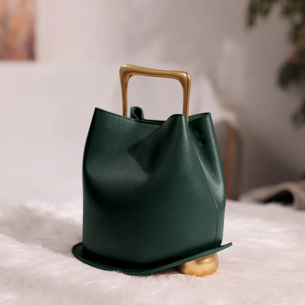 Green handbag with gold handle and base on a light surface