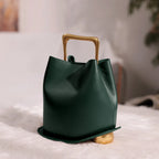 Green handbag with gold handle and base on a light surface