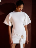 Woman wearing a white dress with a decorative brooch against a dark background