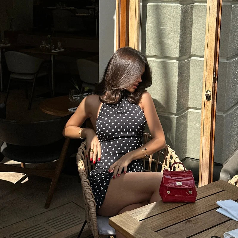 Woman in a polka dot dress sitting at an outdoor cafe table.