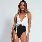 Woman wearing a white and black swimsuit with floral details on a plain background