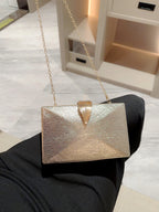 Gold handbag with a chain strap on a black surface
