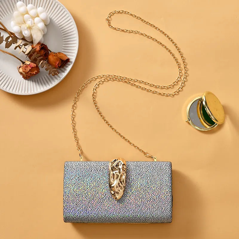 Silver clutch with gold chain and decorative clasp on a beige background