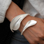 Silver leaf-shaped bracelet on a wrist with a neutral background