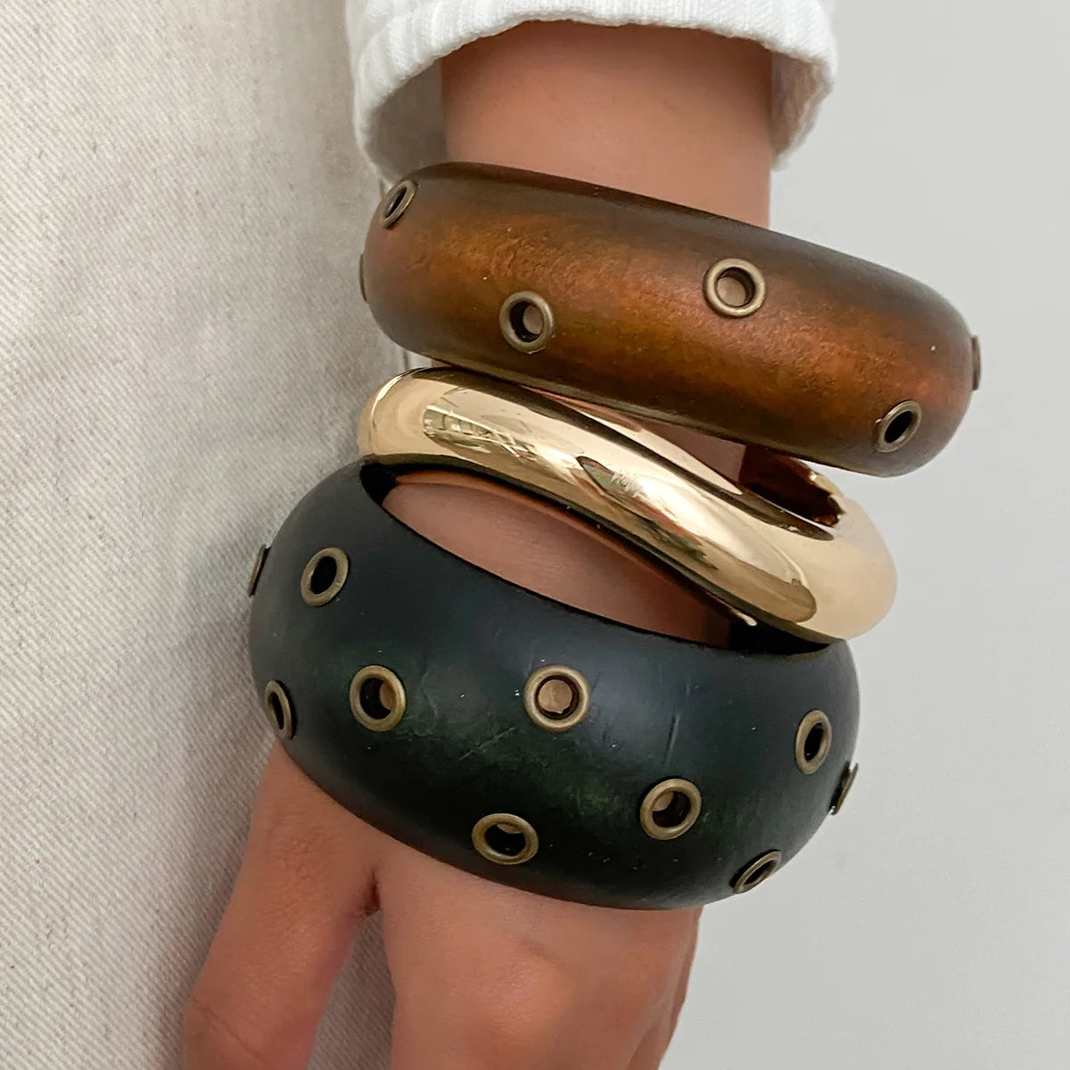 Stack of three metallic bangles on a person's wrist against a neutral background