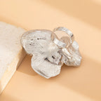 Silver butterfly-shaped ring on a beige stone background