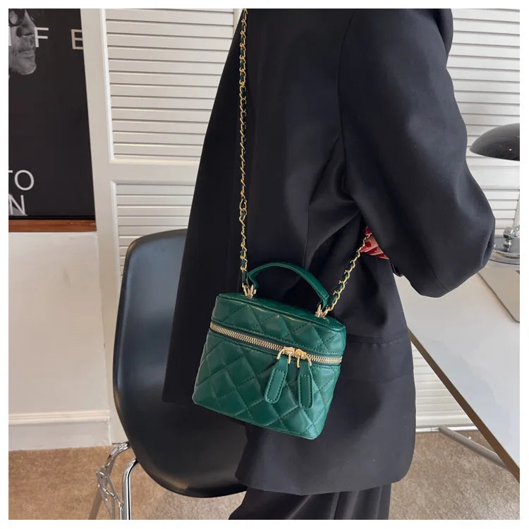 Person wearing a dark coat with a green quilted handbag featuring a gold chain strap.