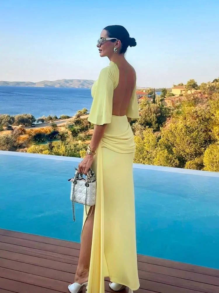 Woman in a yellow dress standing by an infinity pool with a scenic view.