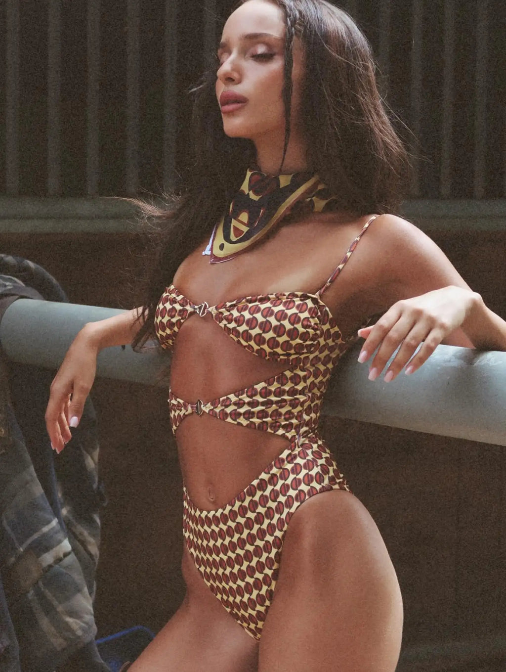 Woman wearing a patterned swimsuit leaning against a railing.