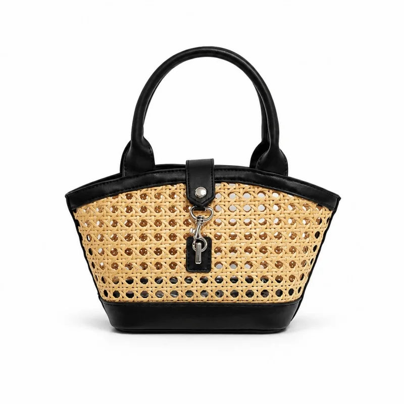 A structured handbag with a natural woven cane body and black faux-leather trim, featuring dual top handles, a front strap closure, and a hanging key charm on a white background.