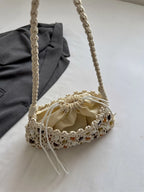 A cream macrame shoulder bag with a drawstring pouch, resting on a white surface next to a dark gray fabric prop.