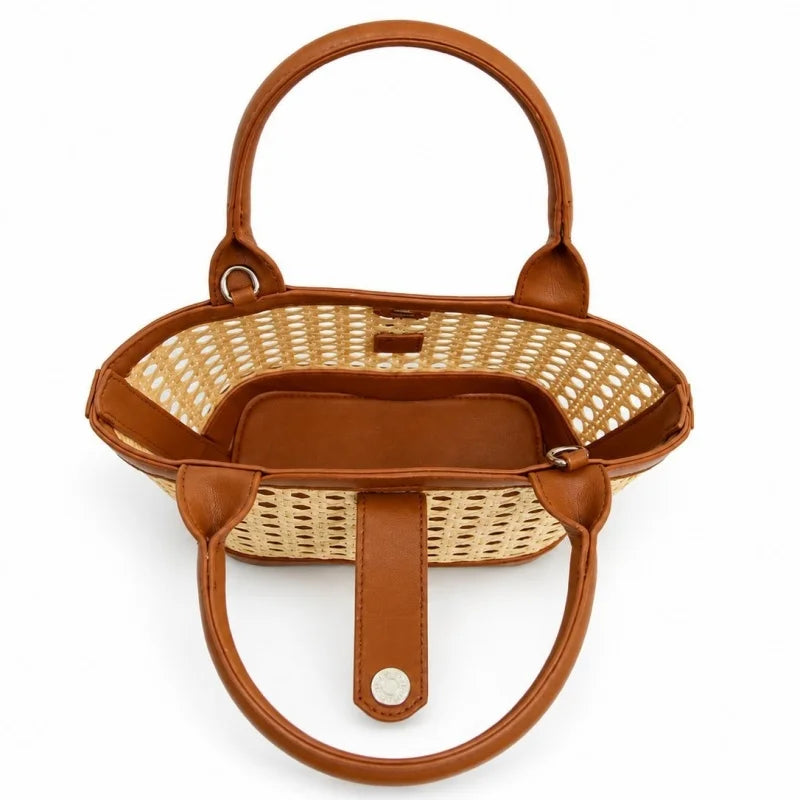 A top-down view of a small woven straw basket handbag with brown leather handles and trim, set against a plain white background.