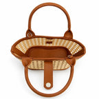 A top-down view of a small woven straw basket handbag with brown leather handles and trim, set against a plain white background.