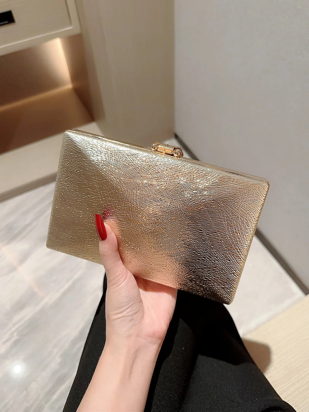 Hand holding a gold clutch against a neutral background