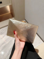 Hand holding a gold clutch against a neutral background