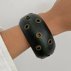 Black wristband with circular holes on a person's arm against a light background