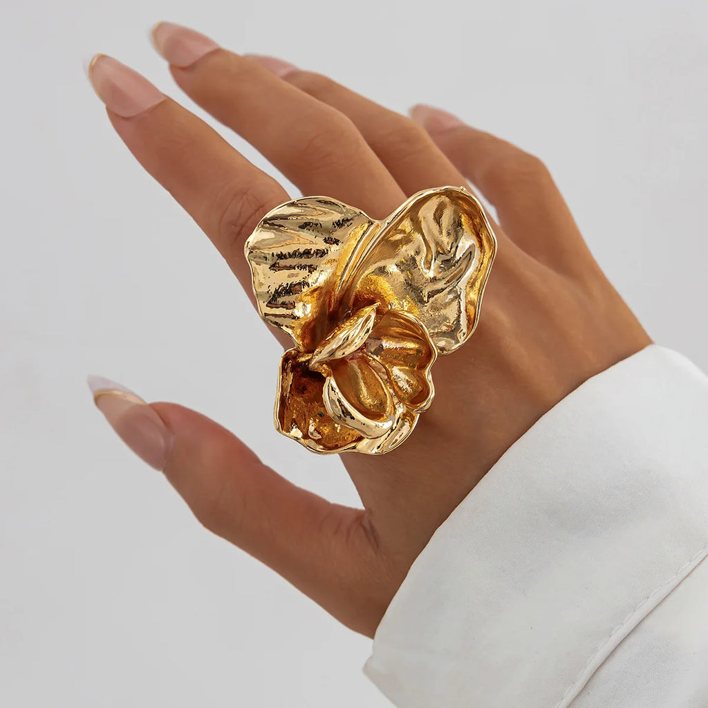 Gold flower-shaped ring on a hand against a neutral background