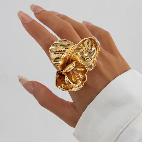 Gold flower-shaped ring on a hand against a neutral background