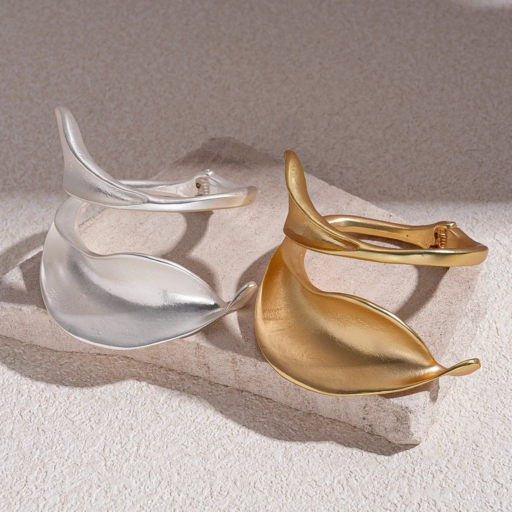 Gold and silver leaf-shaped earrings on a textured surface with a neutral background