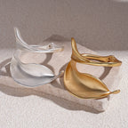 Gold and silver leaf-shaped earrings on a textured surface with a neutral background
