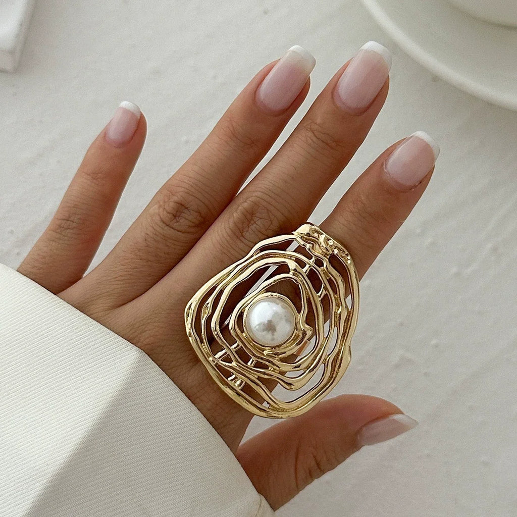 Gold ring with a pearl on a hand against a neutral background