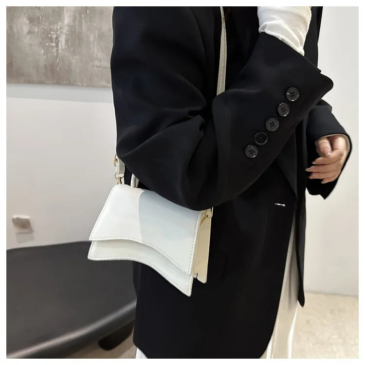 Person wearing a black coat with white buttons, holding a white handbag.