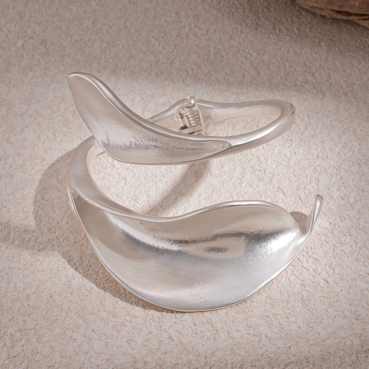 Silver bracelet with a leaf design on a textured beige surface