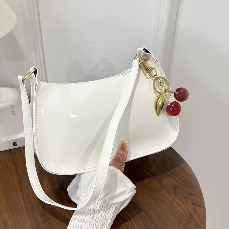 White handbag with a decorative keychain held by a hand on a wooden surface.