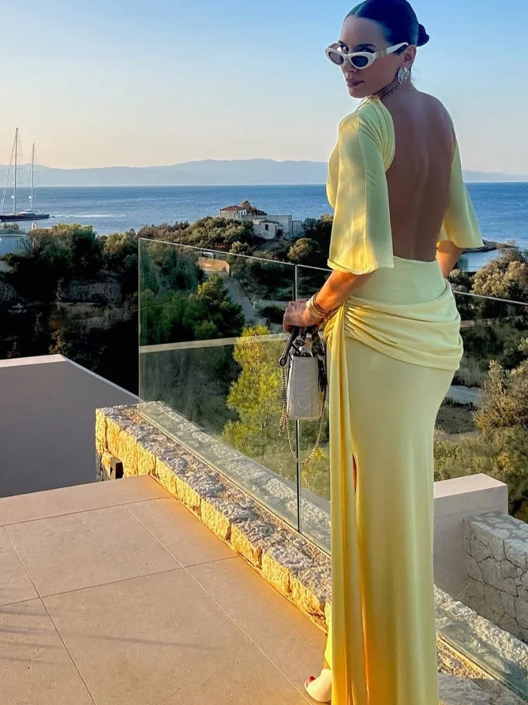 Woman in a yellow dress standing on a balcony with a scenic view of the sea.