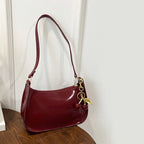 Red handbag with a gold charm on a wooden surface against a white wall