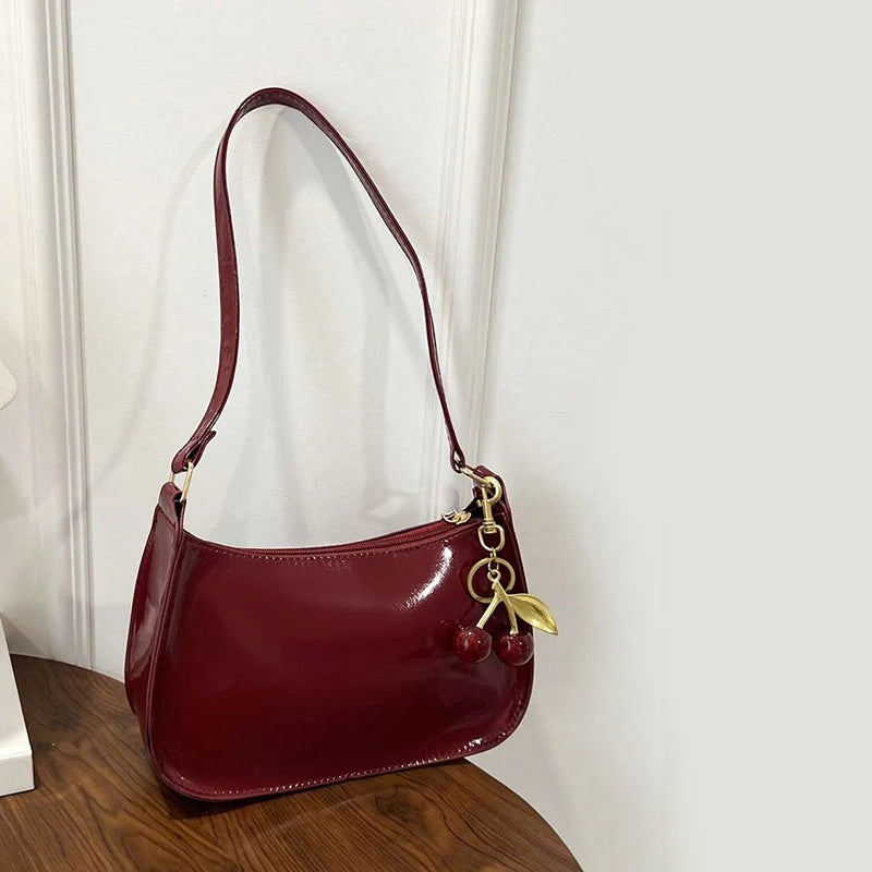 Red handbag with a gold charm on a wooden surface against a white wall