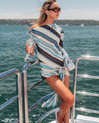 Woman on a boat wearing a striped cover-up with water in the background