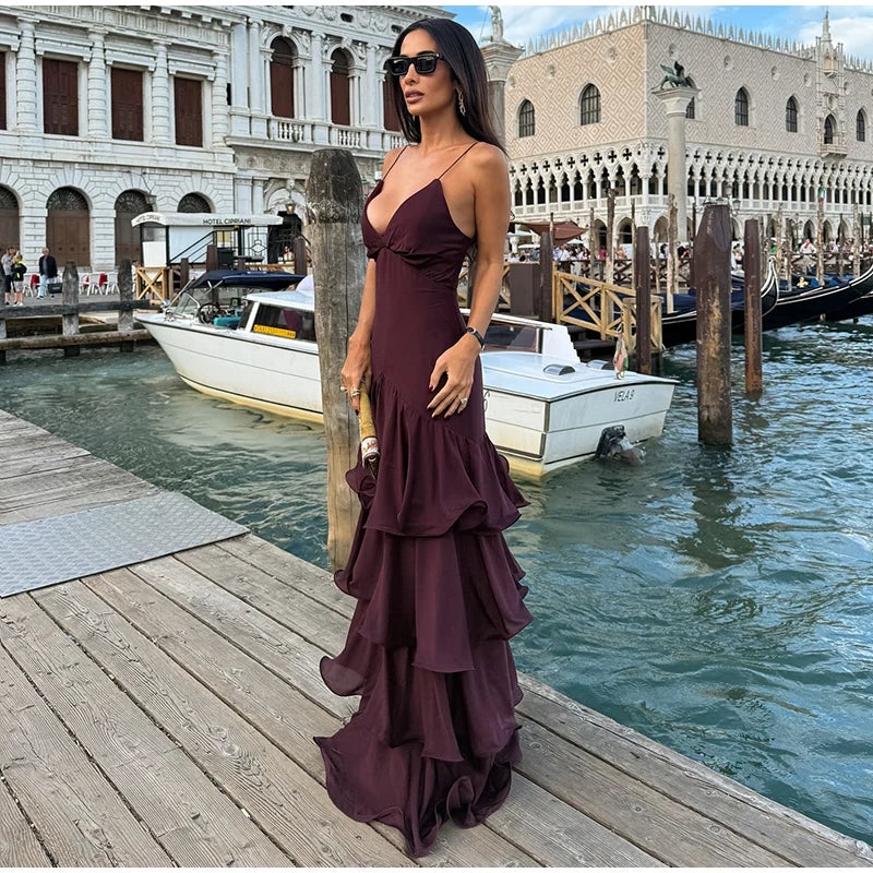 Woman in a purple dress standing on a dock with boats and historic buildings in the background