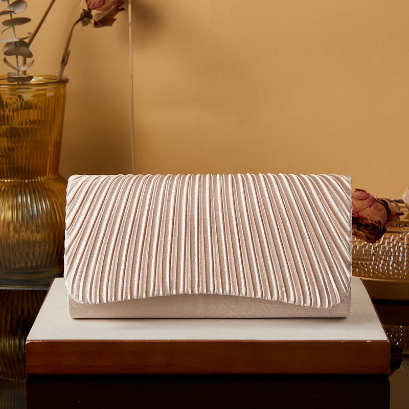 Beige clutch bag with striped pattern on a wooden surface against a beige wall.